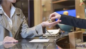 Hotel receptionist handing a physical room key with a keychain to a guest checking in at the front desk.