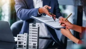 Property expert assisting a client with real estate paperwork and contract signing beside commercial building models.